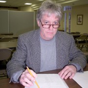 Gray-haired man with glasses at a desk with pencil and paper